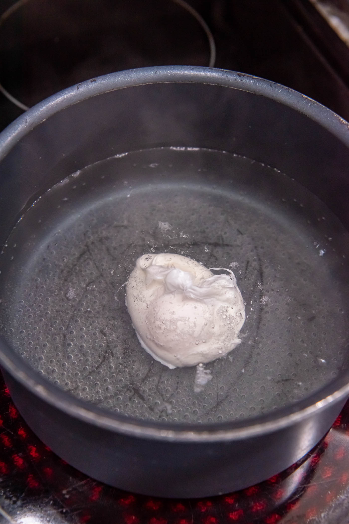 Cooking poached egg in pot of barely boiling water.