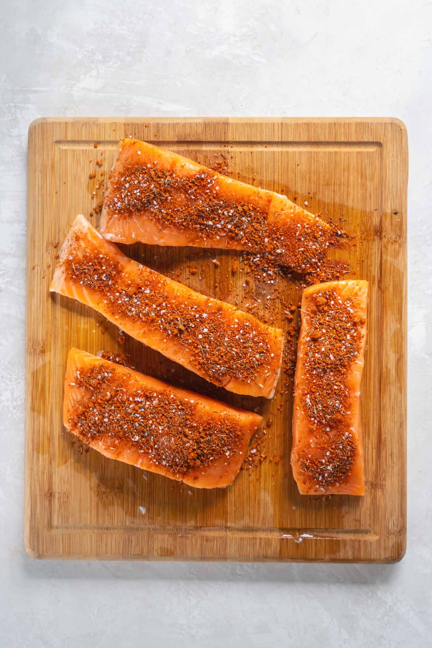 Seasoning sprinkled over four salmon fillets on a cutting board.