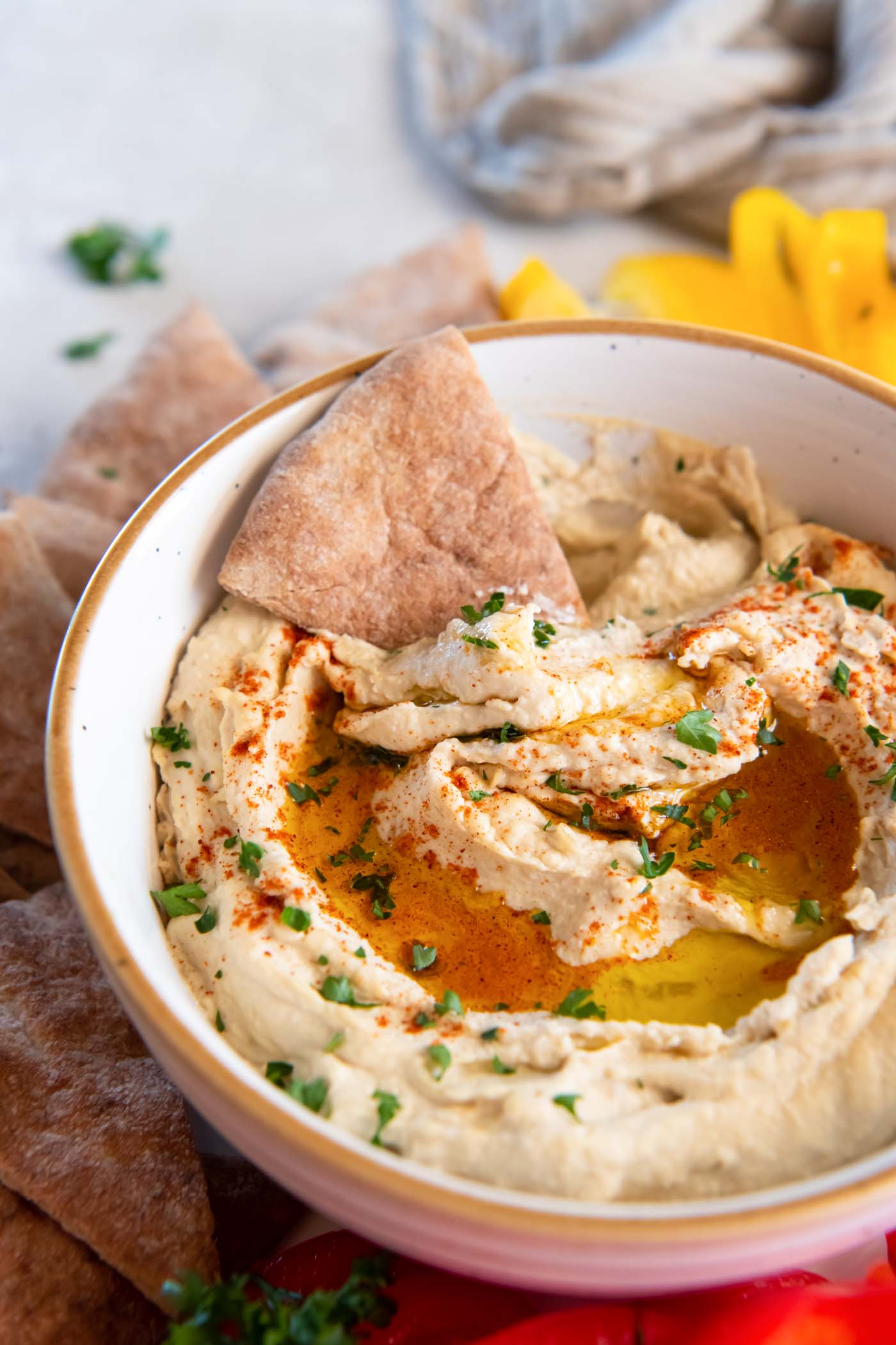 Bowl of hummus with pita bread triangle dipped in it.