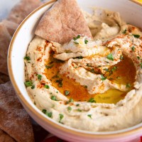 Bowl of hummus with pita bread triangle dipped in it.
