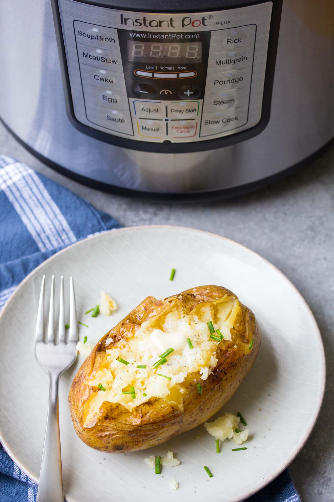 Plated baked potato topped with salt, pepper, butter and chives, with instant pot in the background.