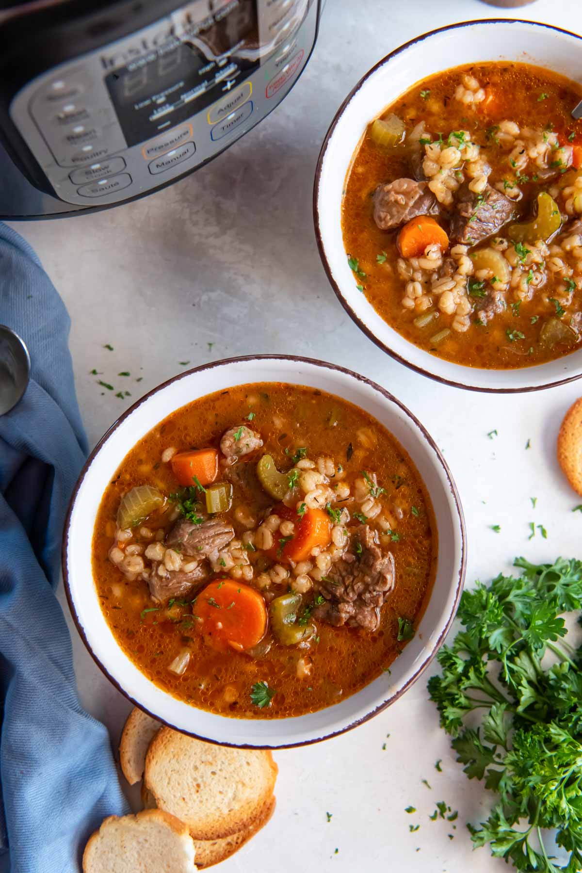 Two bowls of instant pot beef barley soup with instant pot in the background.