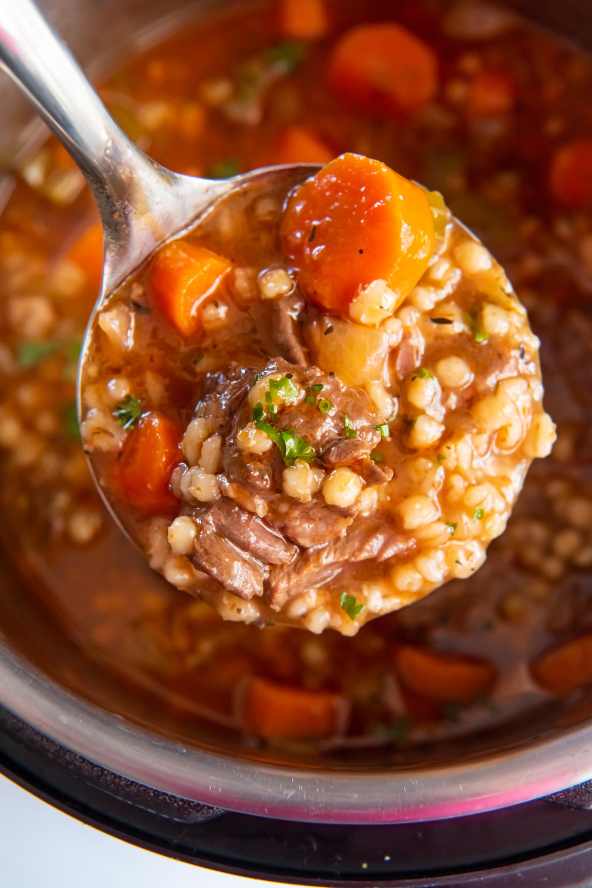Beef Barley soup on a ladle held over Instant Pot.