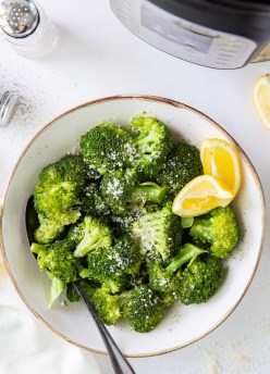 bowl of broccoli with grated parmesan cheese and lemon wedges, with instant pot in background