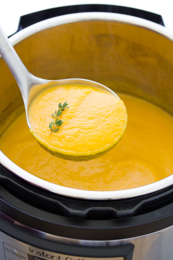 A ladle full of creamy butternut squash soup scooped from an Instant Pot, garnished with thyme.