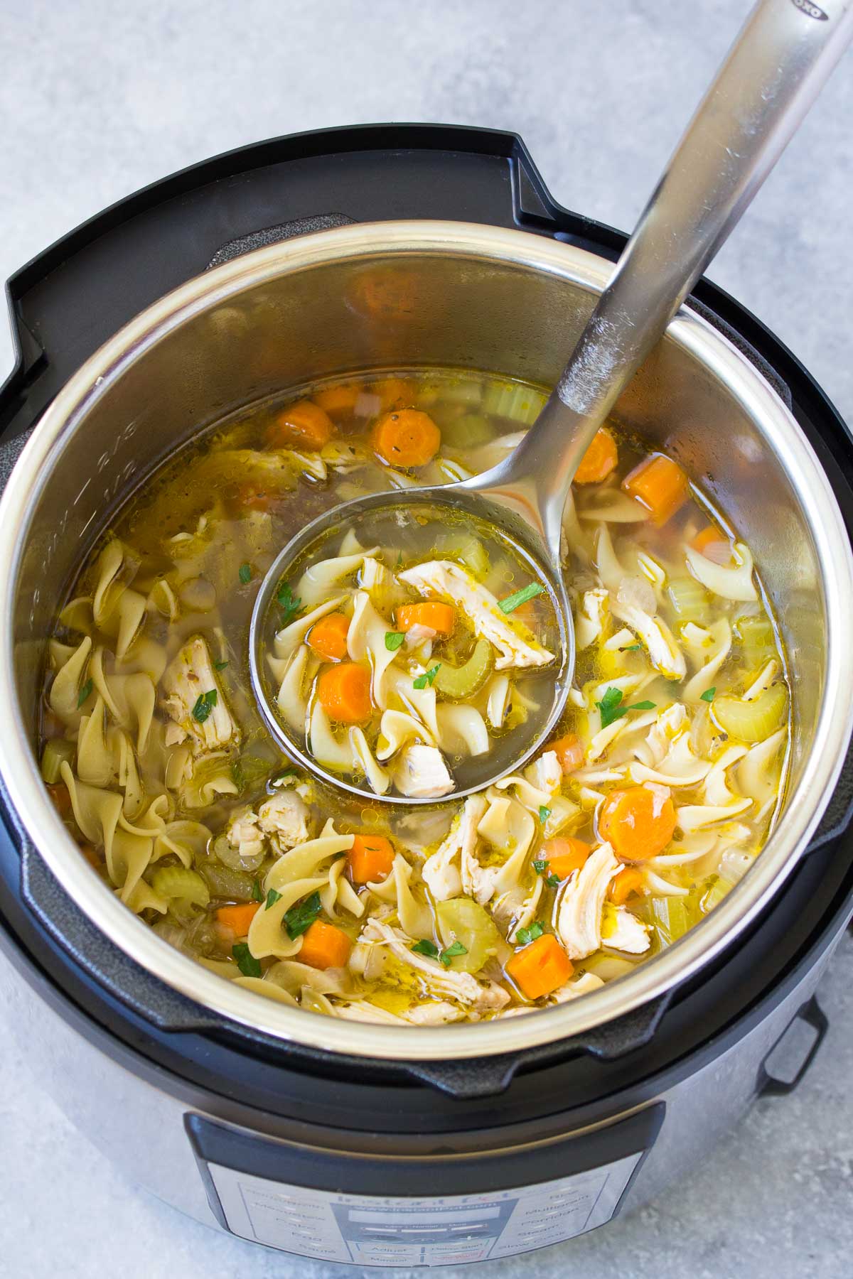Chicken noodle soup in an instant pot with a ladle.