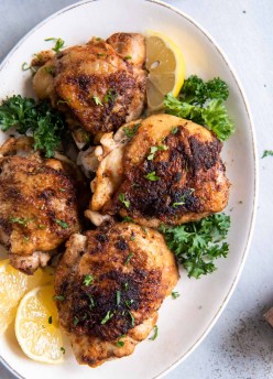 Instant Pot chicken thighs on a serving plate with lemon wedges and parsley.