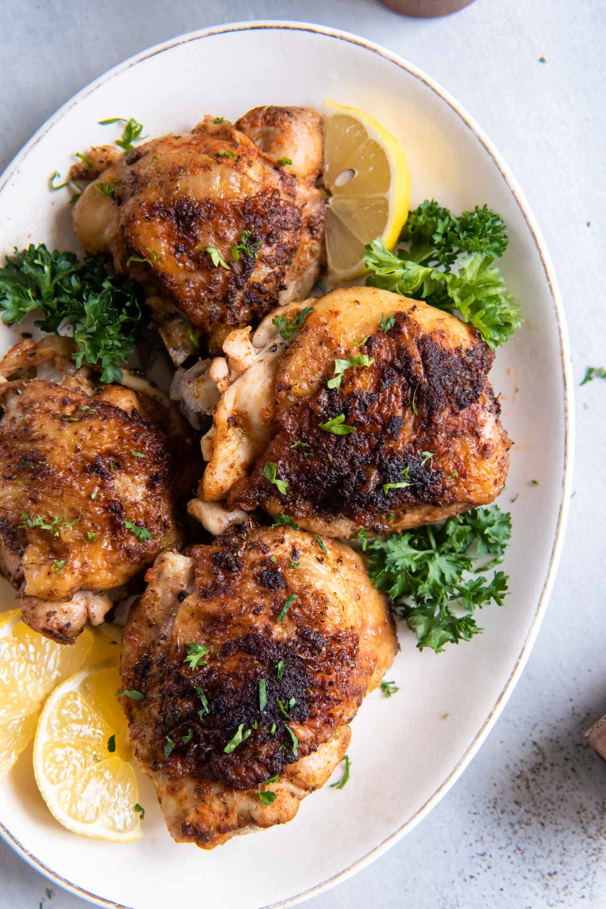 Bone in Instant Pot chicken thighs on a serving platter with parsley and lemon wedges.