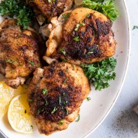Instant pot chicken thighs on a serving plate with parsley and lemon wedges.