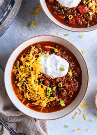 Instant pot chili served in two bowls with toppings, with Instant Pot in the background.