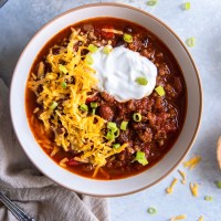 Instant pot chili in a bowl topped with sour cream, cheddar cheese and green onions.