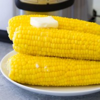 Four ears of corn stacked on a plate with melty butter.
