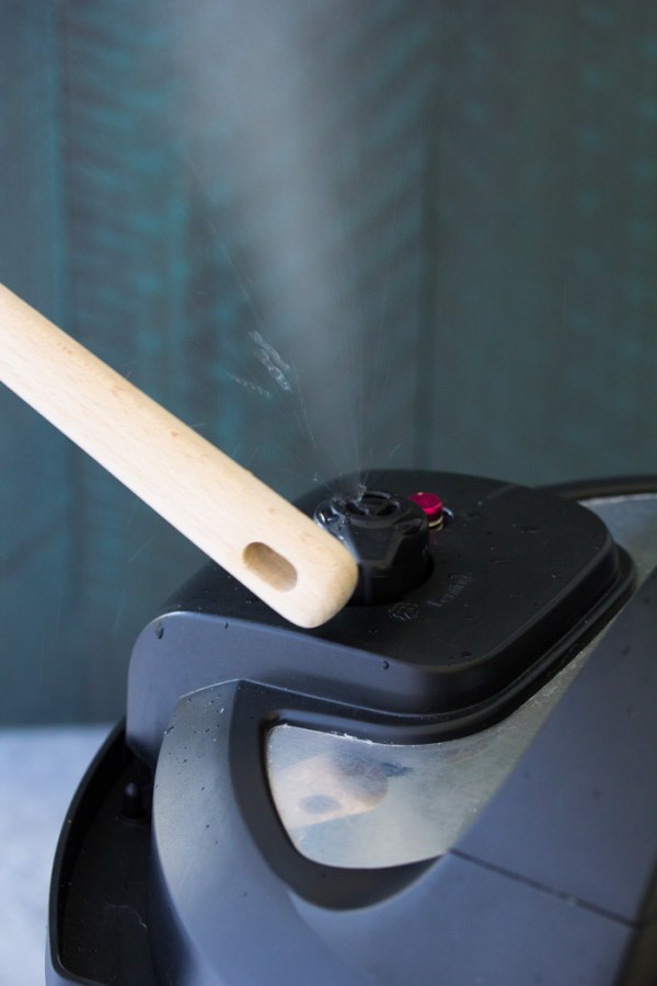 Opening the Instant Pot steam release valve with the handle of a wooden spoon.