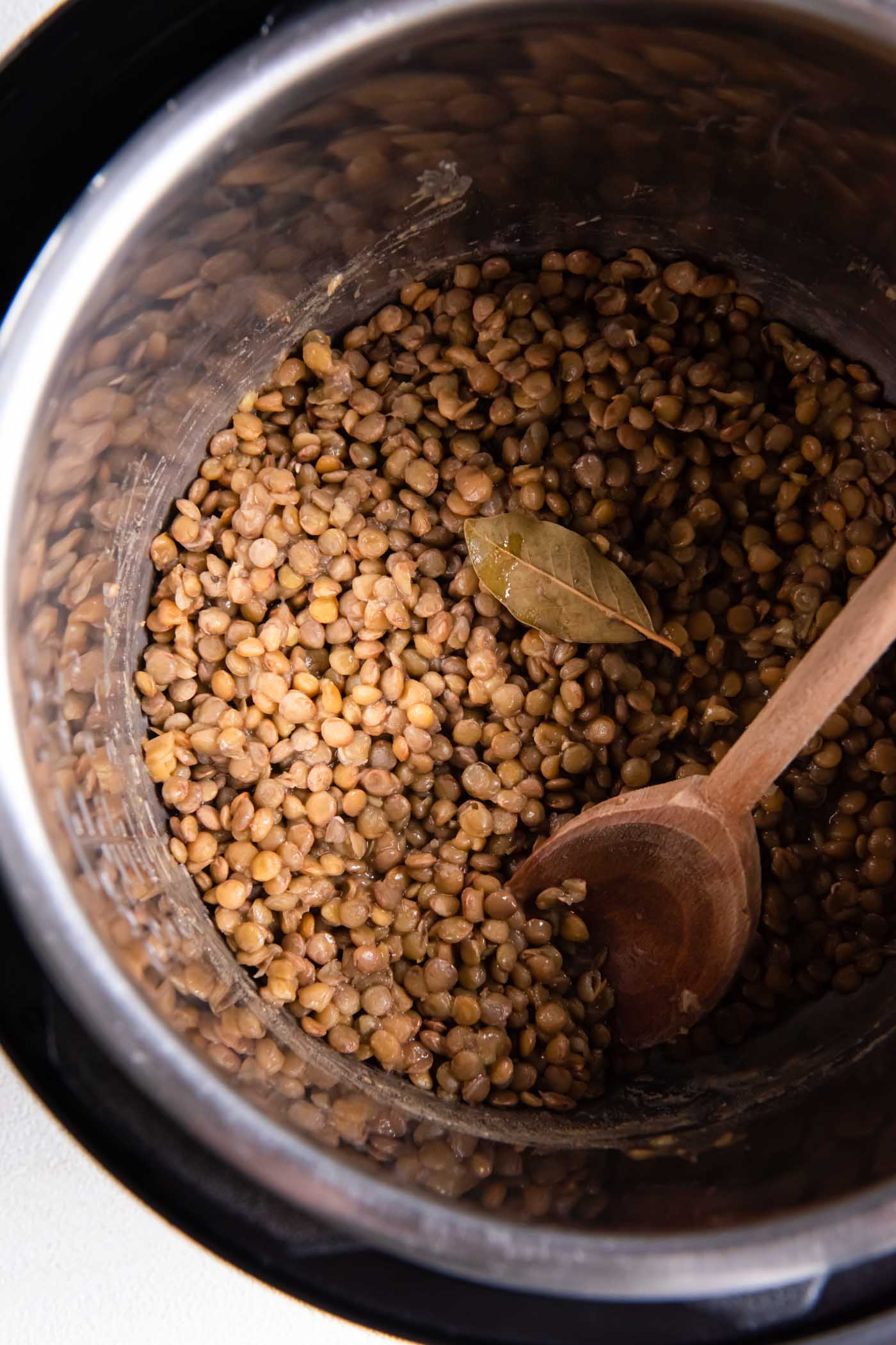 Cooked lentils in instant pot with bay leaf and wooden spoon.