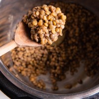 Cooked lentils on wooden spoon held over instant pot.
