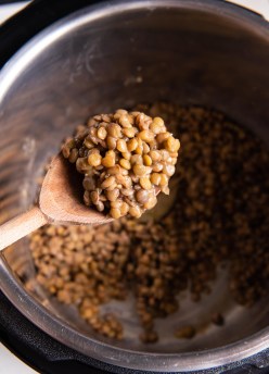 Cooked lentils on wooden spoon held over instant pot.