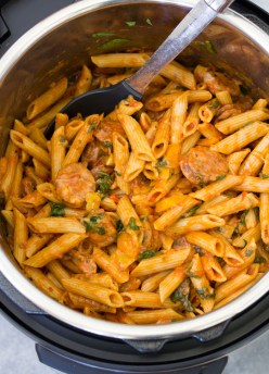 Instant Pot pasta with sausage and veggies in an Instant Pot pressure cooker, with a serving spoon.