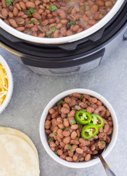 Overhead photo of pinto beans recipe in a white bowl, with an Instant Pot, tortillas and cheese.