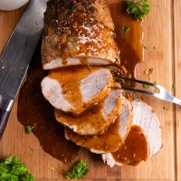 Sliced instant pot pork loin on a cutting board with gravy.