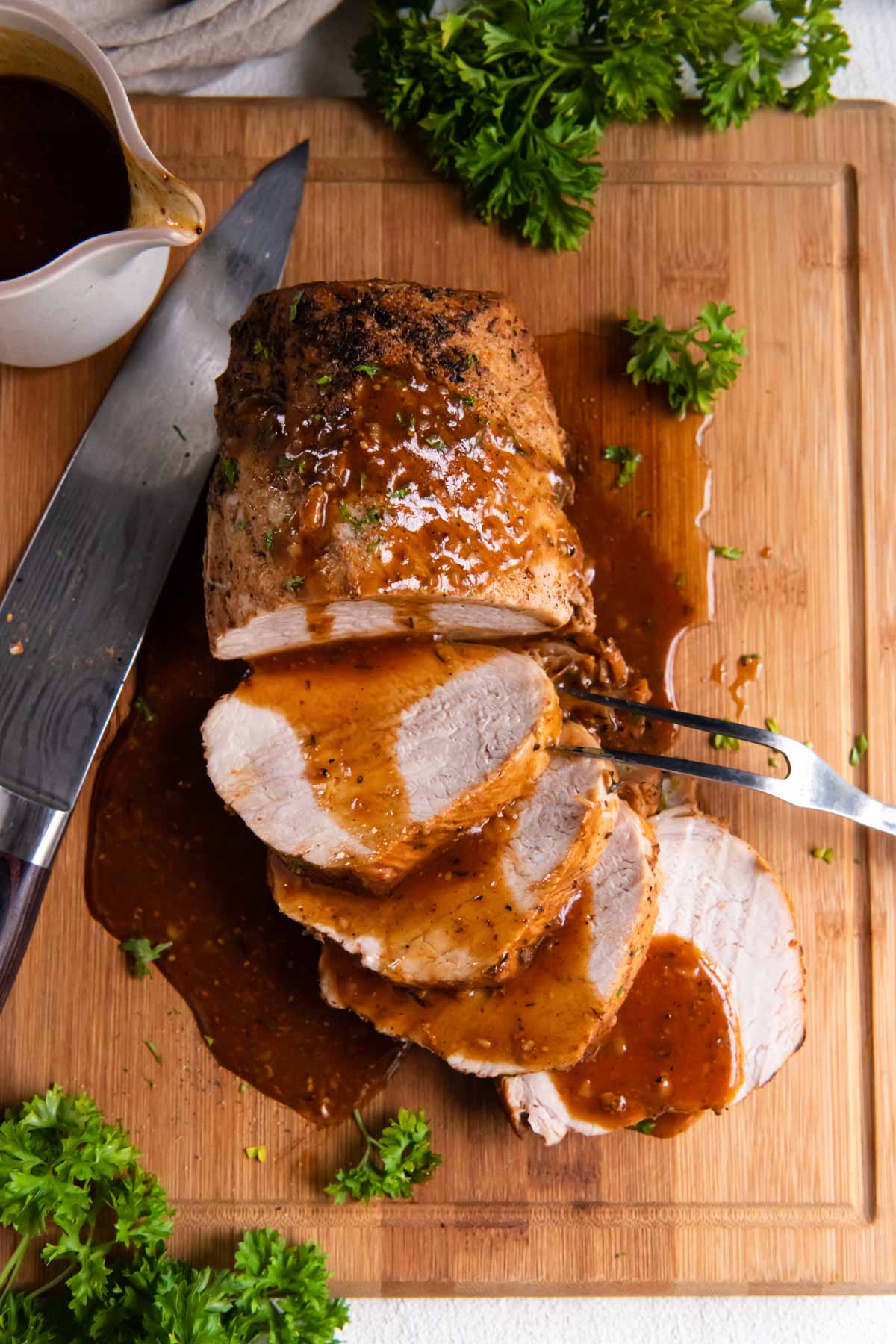 Partially sliced instant pot pork loin on a cutting board with gravy.