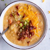 Bowl of instant pot potato soup topped with bacon, shredded cheddar and green onions, with spoon in bowl.