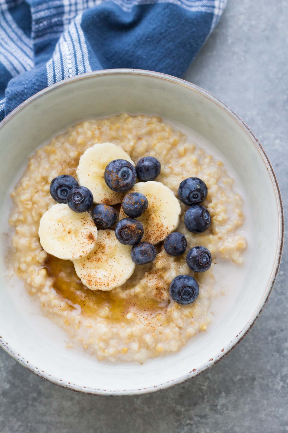 Bowl of steel cut oats topped with maple syrup, sliced banana, blueberries and cinnamon.