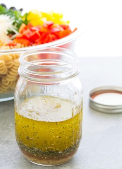 Homemade Italian dressing in a mason jar with pasta salad in the background.