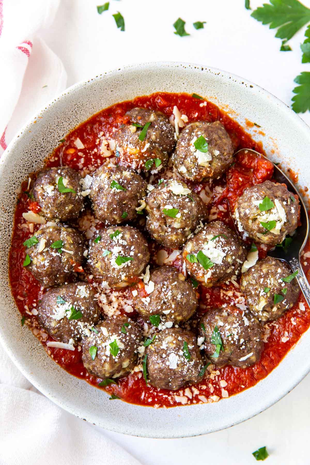 meatballs in a serving dish with marinara sauce, parmesan cheese and parsley