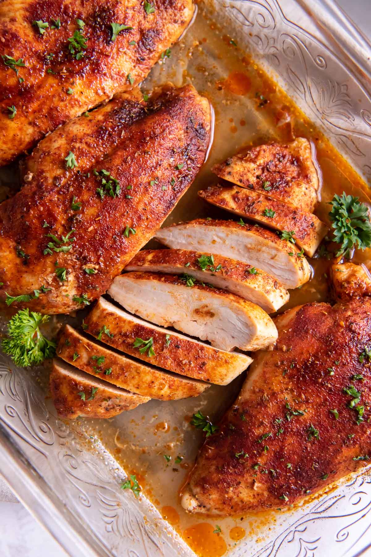 Sliced and whole baked chicken breasts in baking dish.