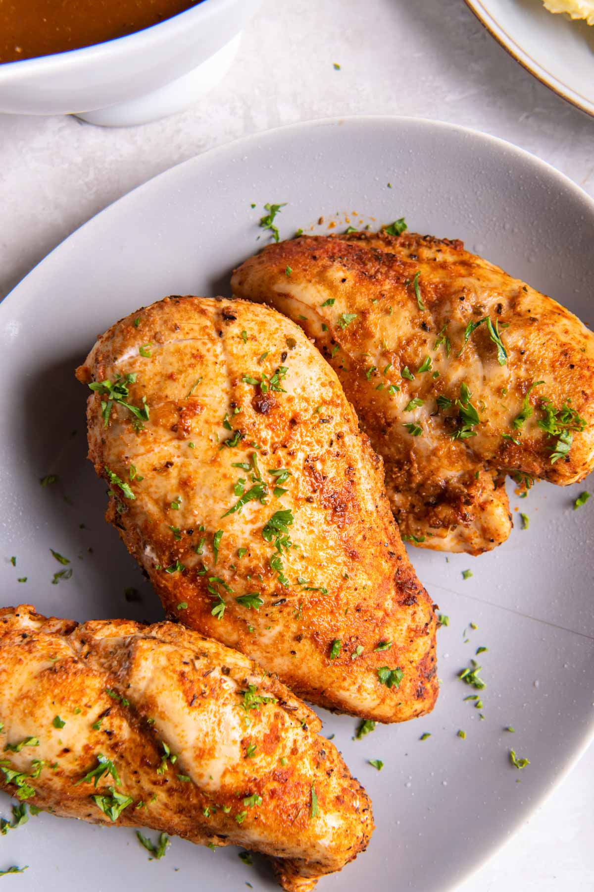 Three cooked chicken breasts on a plate.