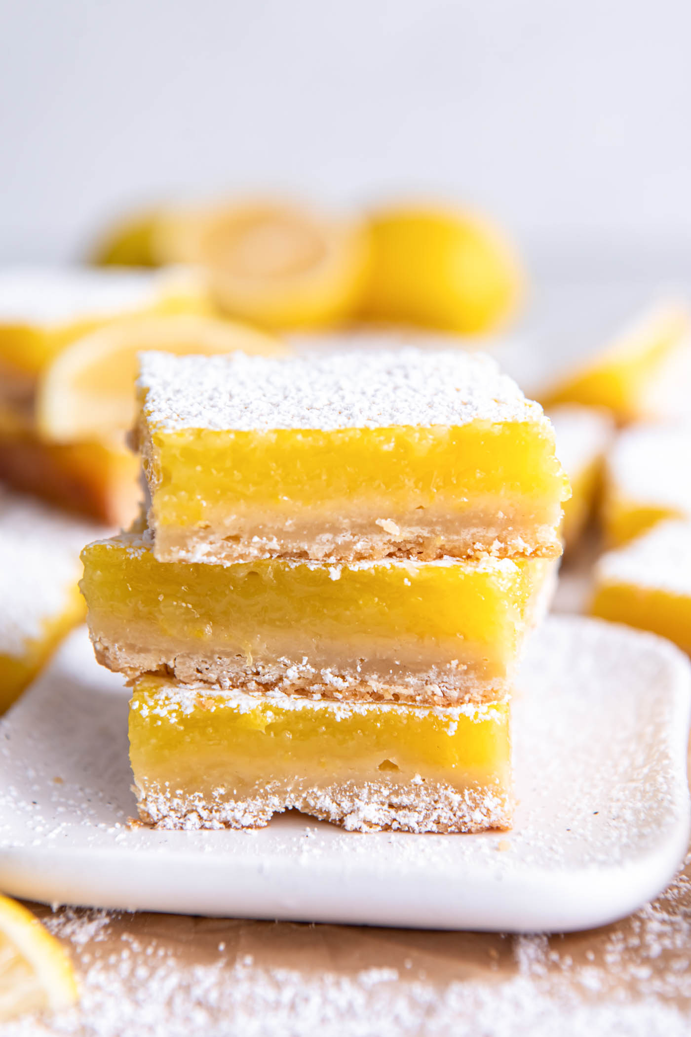 Three lemon bars stacked on a small square plate.