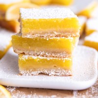 Three lemon bars stacked on a small square plate.