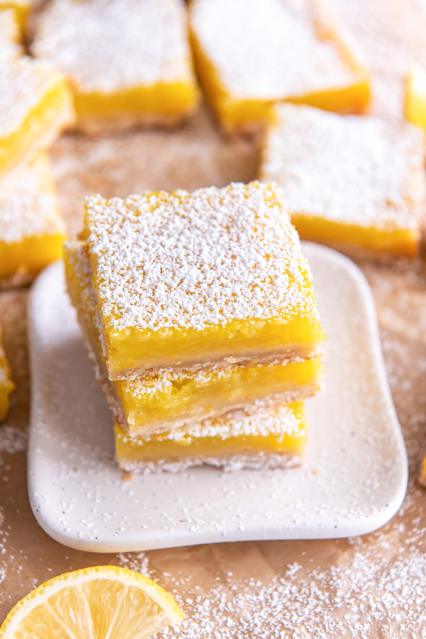 Three lemon bars stacked on a small white plate with powdered sugar on top.