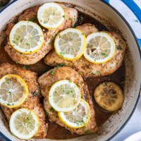 Baked lemon chicken breasts with fresh lemon slices in a braiser pot.