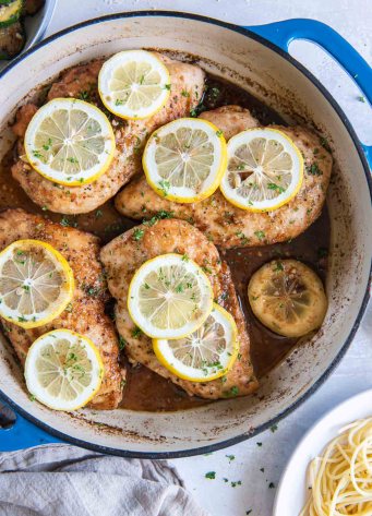 Lemon chicken breasts with fresh lemon slices in a braiser pot.