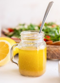 Lemon vinaigrette dressing in a glass jar with a spoon with arugula salad in background..