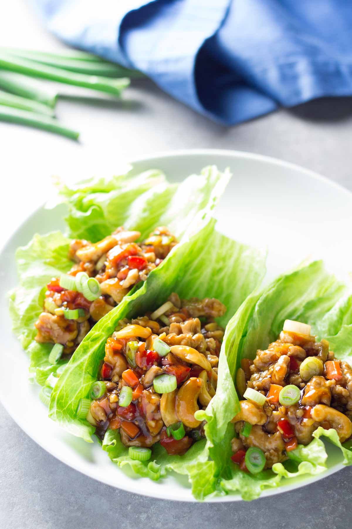 Chicken lettuce wraps with cashews on a white plate with green onions in the background.