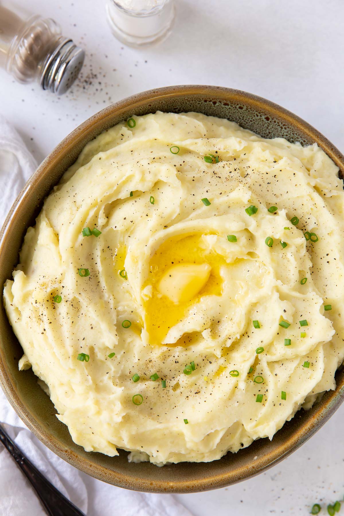 serving dish with mashed potatoes topped with melted butter and chives