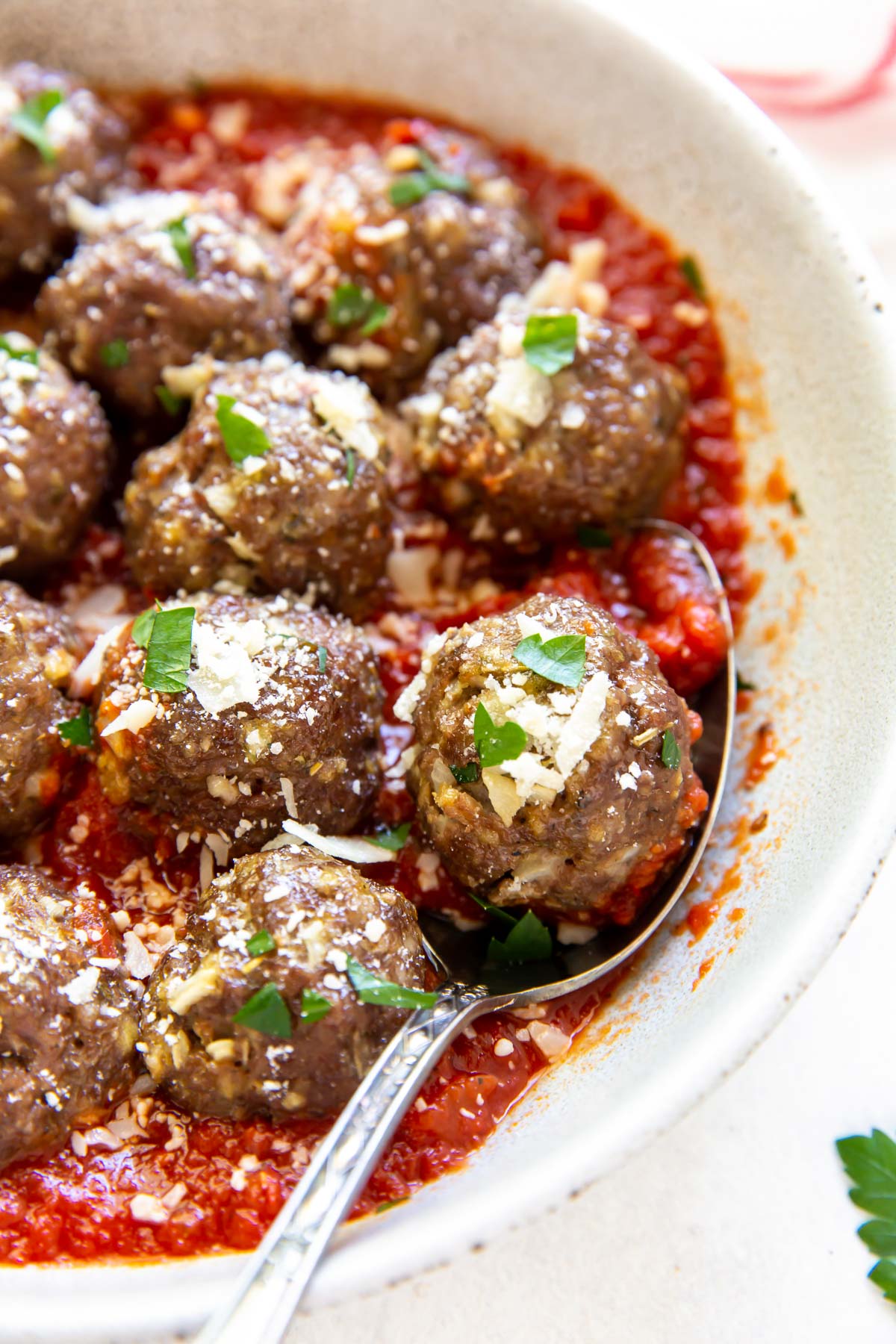 close up of meatballs in a serving dish with marinara sauce, parmesan cheese and parsley, with one meatball on a spoon
