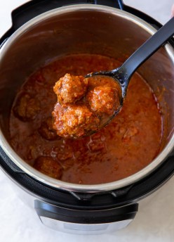 three meatballs on a serving spoon held over an instant pot full of marinara sauce and meatballs