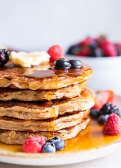Stack of 5 oatmeal pancakes topped with butter, maple syrup and fresh berries.