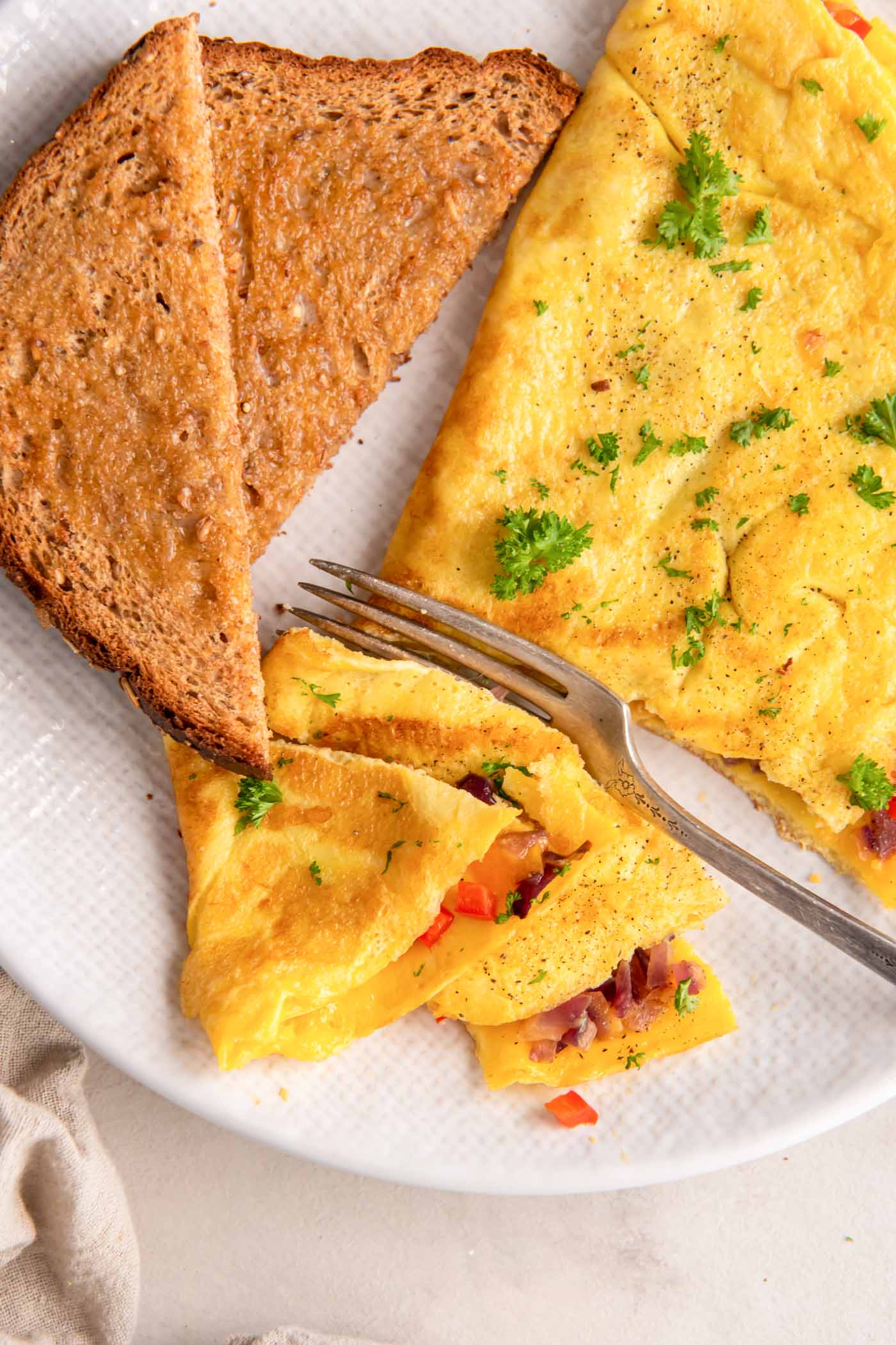 Omelette and buttered toast on a plate with fork and a few bites of omelette cut.