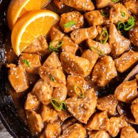 Close up of orange chicken in a skillet garnished with orange wedges.