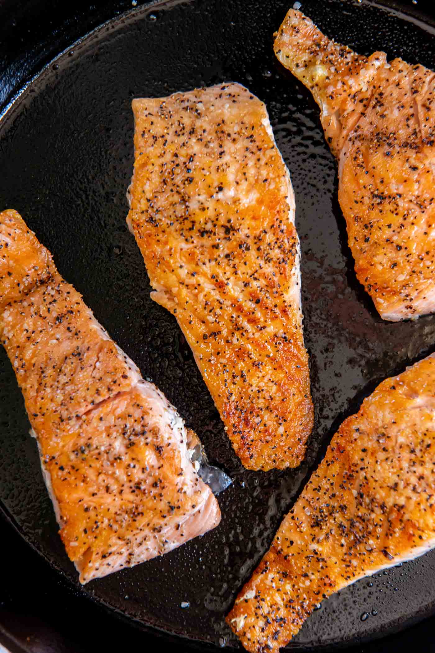 Four cooked salmon fillets in a cast iron skillet.