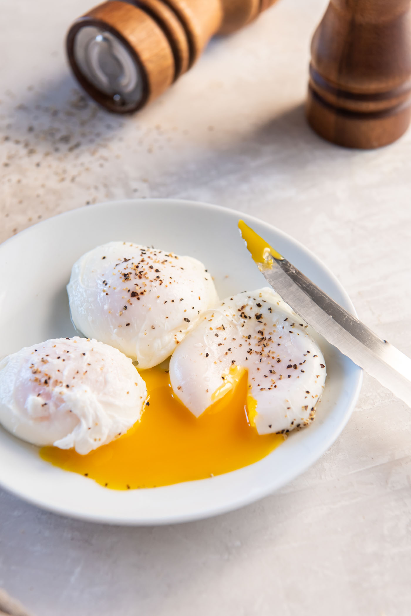 Three poached eggs on a plate with one sliced open so yolk runs out.
