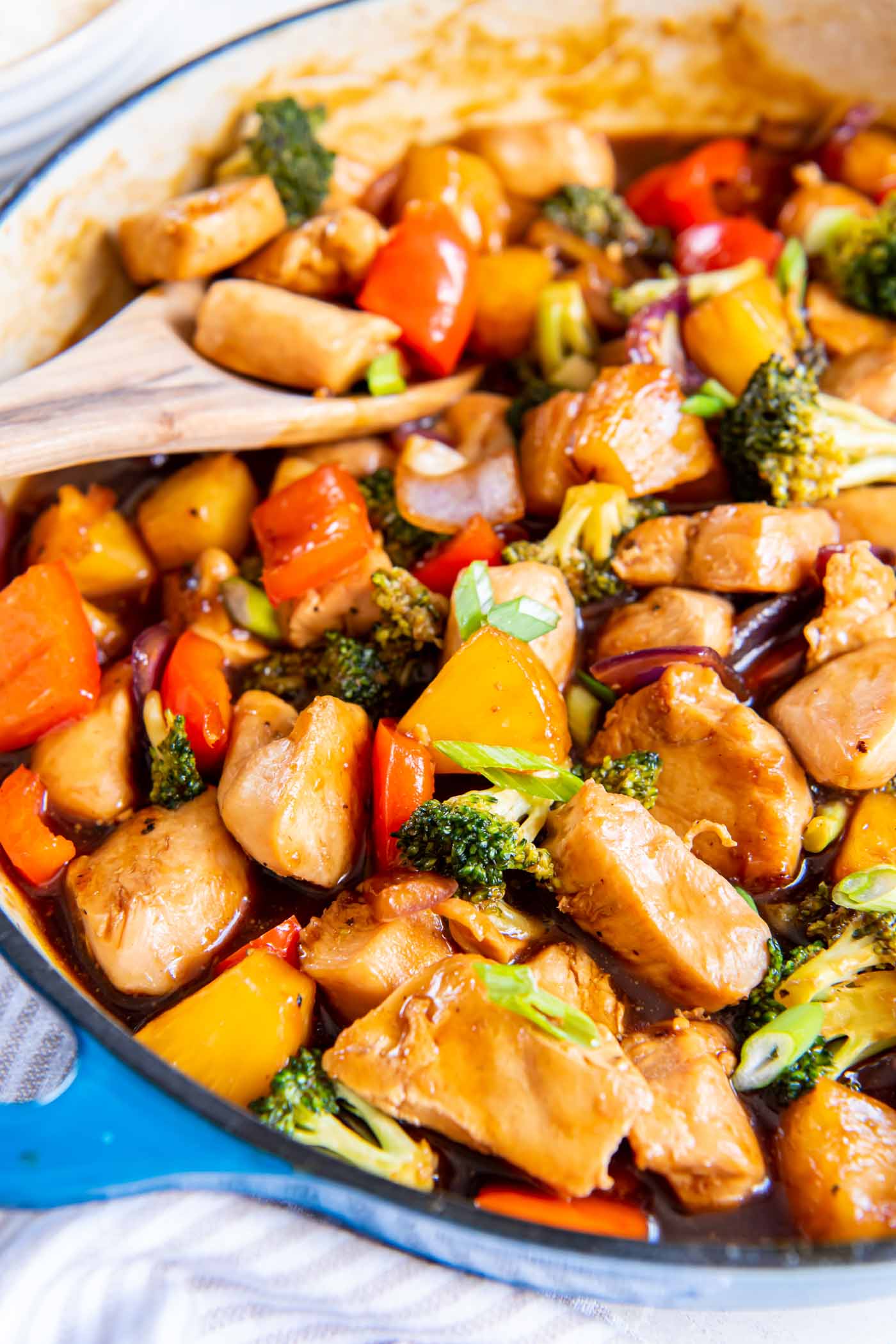 Pineapple chicken in skillet with wooden spoon.