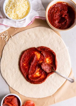 Spreading pizza sauce on rolled out pizza dough.