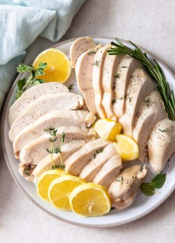 sliced poached chicken on a plate with lemon and herbs