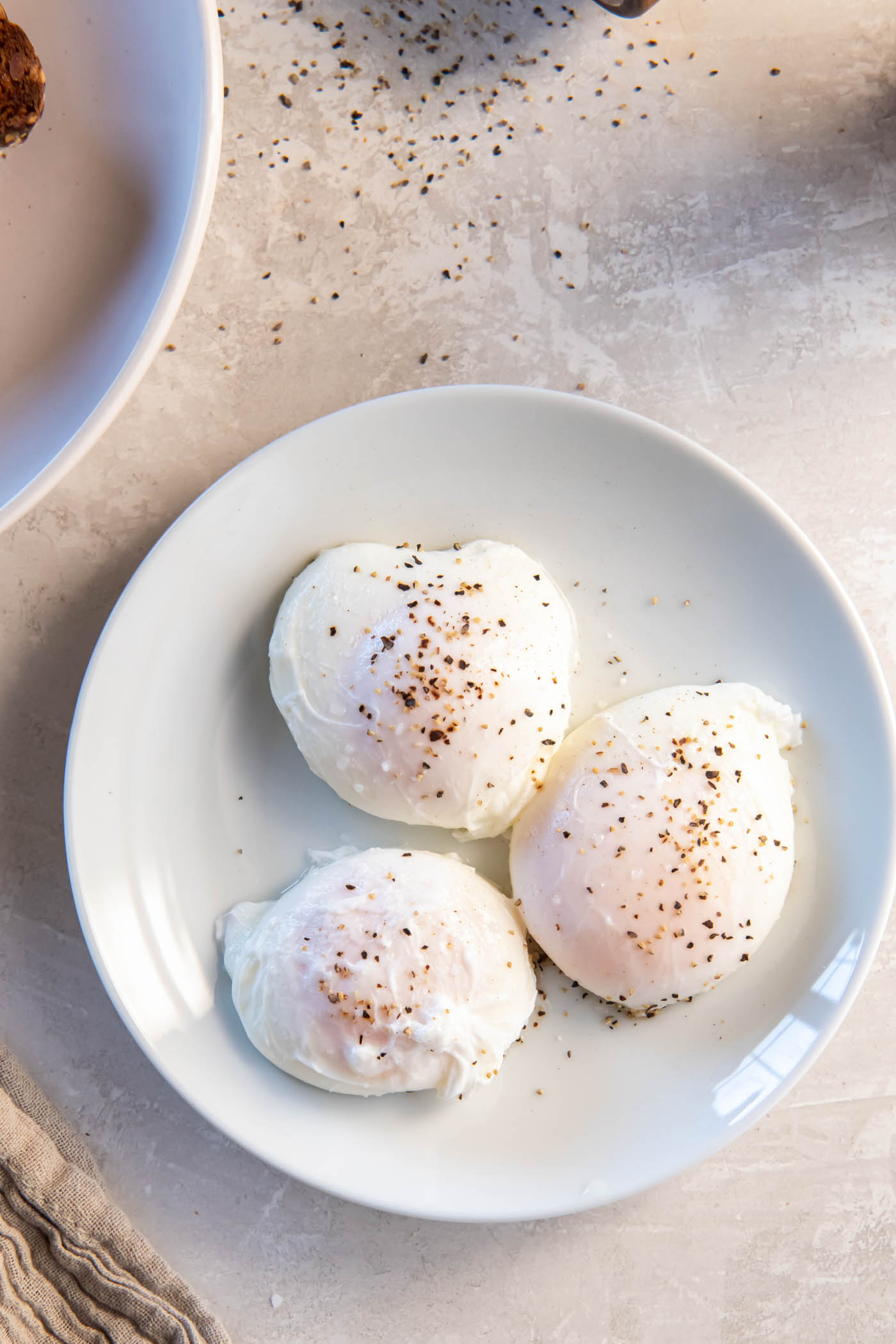 Three poached eggs with salt and pepper on a plate.