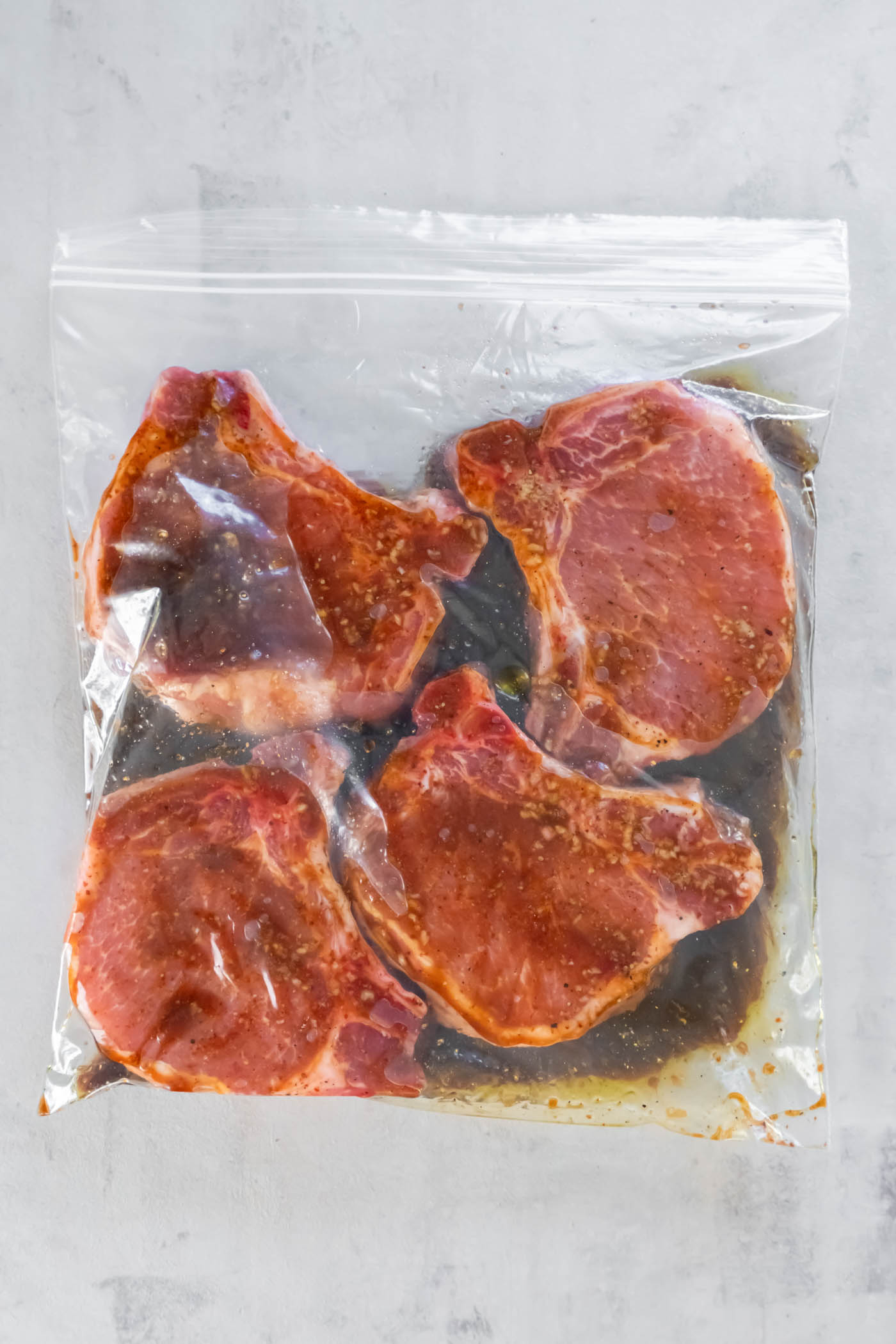 Four bone-in pork chops sealed in a zip-top bag with pork chop marinade.